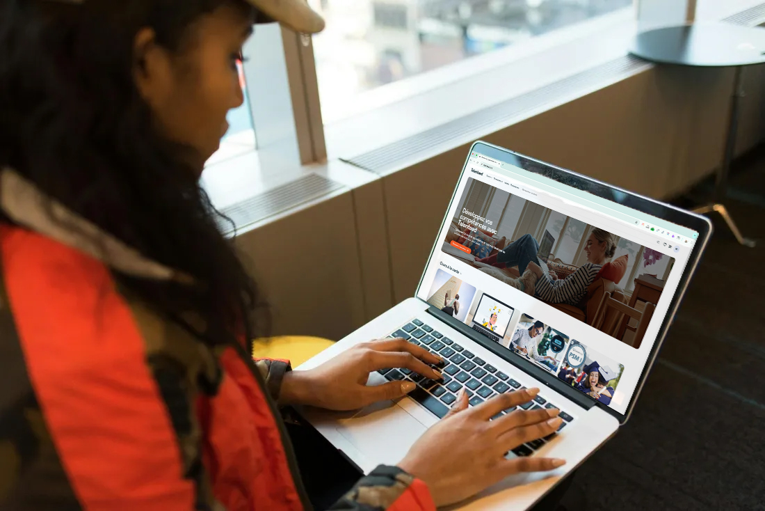 Personne tapant sur un ordinateur portable sur la page d'accueil talenteed.com avec une vue sur la ville.